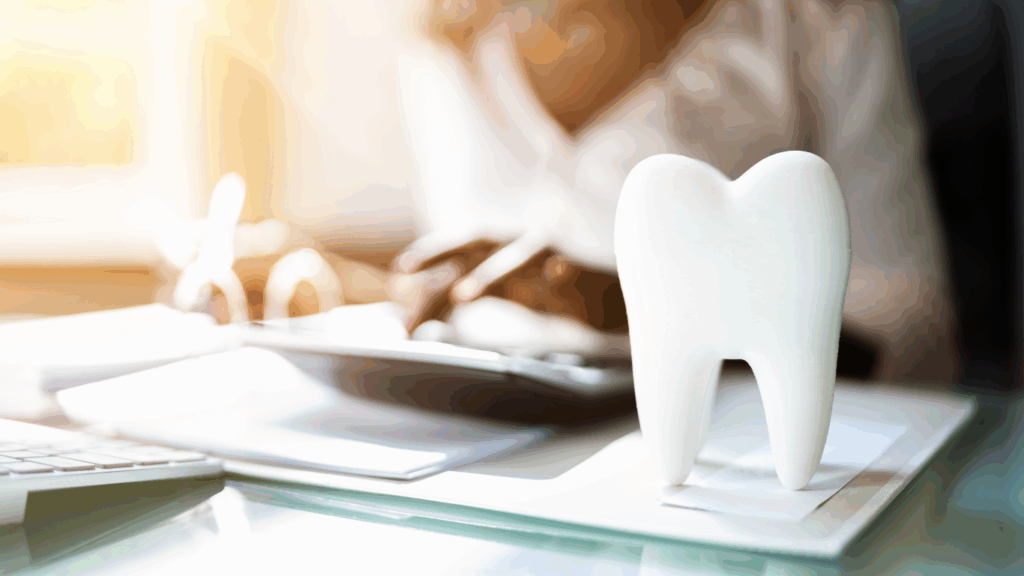 Person calculating insurance at a desk with a tooth on top of the forms